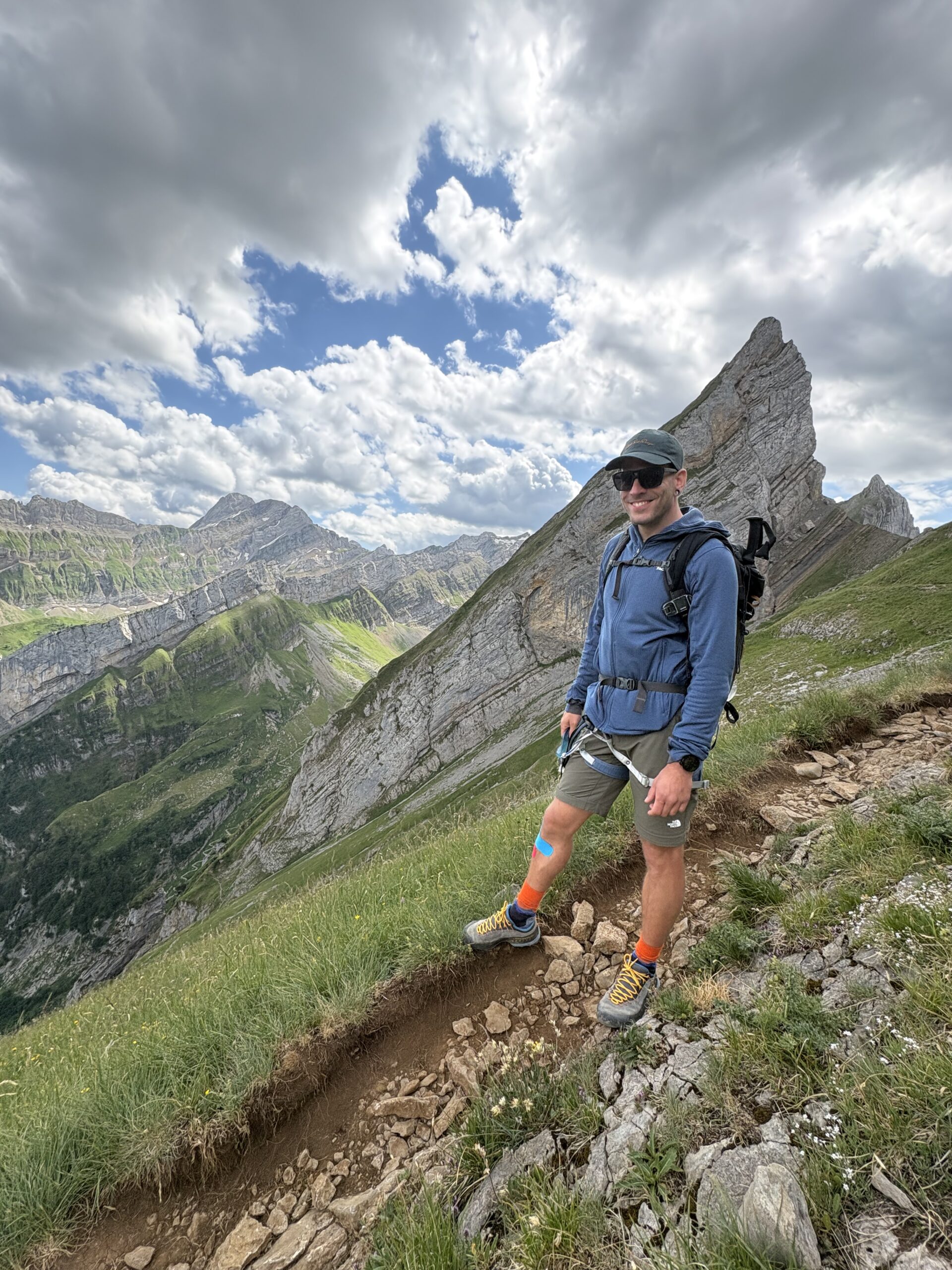 Alex wandert mit Rucksack &uuml;ber einen schmalen Felsgrat, im Hintergrund Wolken und Gipfel